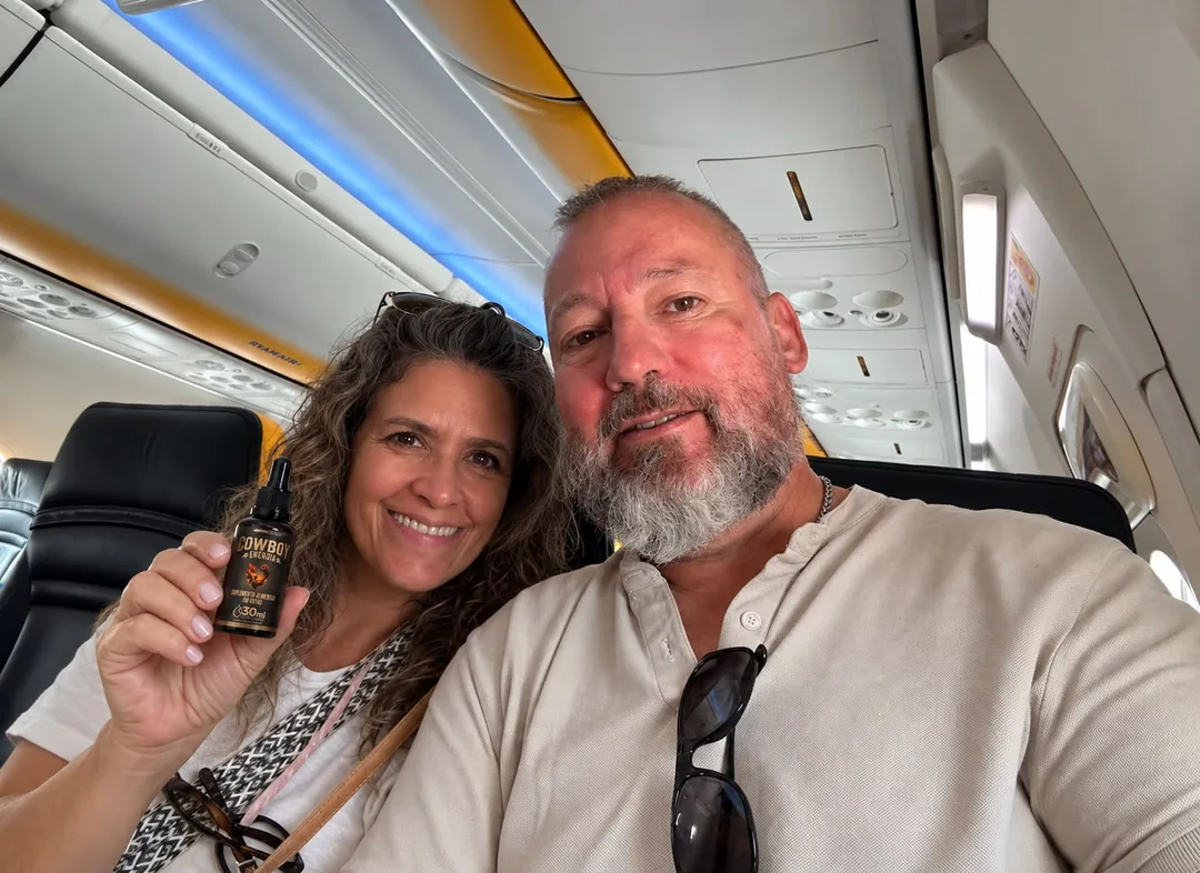 Casal sorrindo dentro de um avião, a mulher segurando um frasco COWBOY Energia